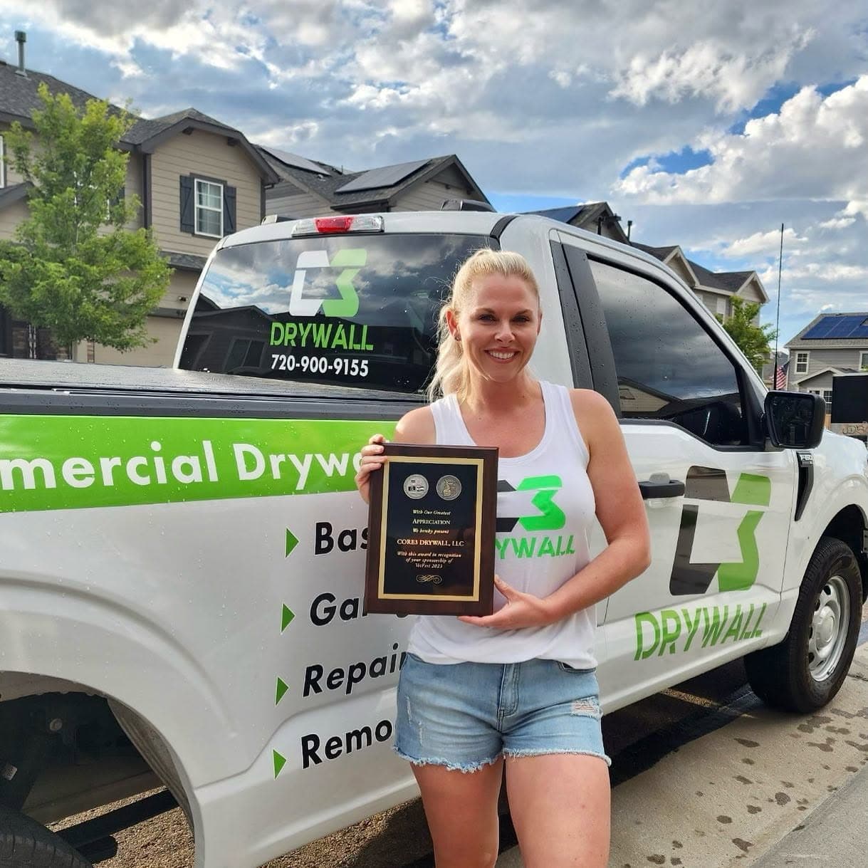 Owner Katie Andrews holding an award recognizing Core3 Drywall's VetFest sponsorship, beside the C3 Drywall truck.